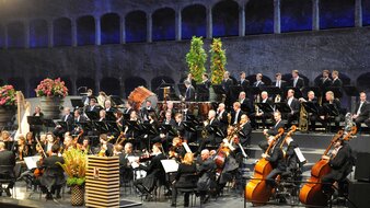 Orchester auf einer Bühne, im Hintergrund steinerne Arkaden | © Tourismus Salzburg
