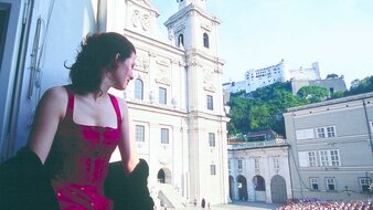 Frau am Fenster sitzend und blickt auf die Bühne am Domplatz, wo das Stück "Jedermann" aufgeführt wird | © SalzburgerLand Tourismus