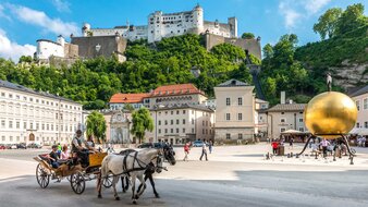 Platz mit Pferdekutsche und Kunstwerk - eine große goldene Kugel, worauf eine Figur steht - im Hintergrund Festungsberg mit Festung | © Tourismus Salzburg/Günter Breitegger