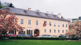 Apricotfarbenes einstöckiges Gebäude mit blühenden Magnolienbäumen im Vordergrund | © Tourismus Salzburg