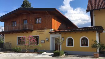 Gelbes Haus mit Holzfassade beim Obergeschoss, blühender Magnolienbaum davor | © Fischachtubn