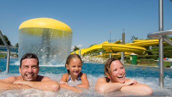 Zwei Erwachsene und ein Kind lehnen am Rand des Schwimmbeckens | © Tourismusverband Bergheim/Bryan Reinhart
