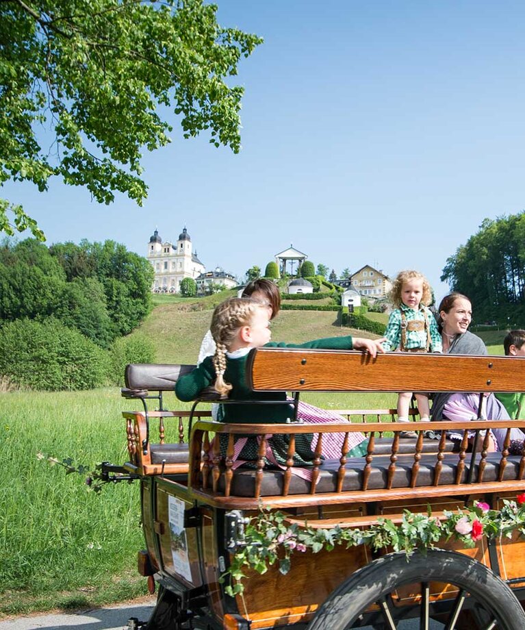 Mit Blumen geschmückte Pferdekutsche in welcher in Tracht gekleidete  Kinder und Erwachsene sitzen | © www.hannelore-kirchner.com