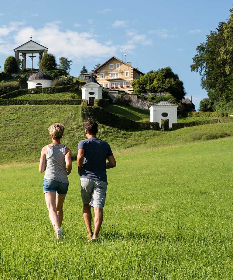 Pärchen auf Wiese und läuft Richtung Hügel mit Kapellen und Kirche | © Tourismusverband Bergheim/Bryan Reinhart