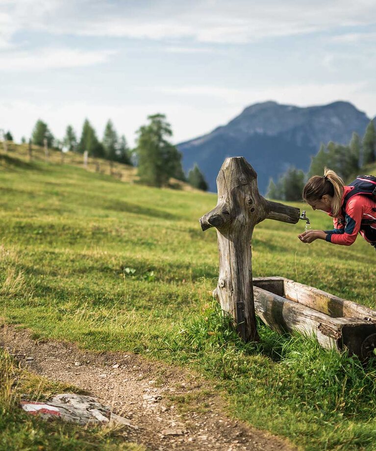 Frau erfrischt sich bei einem Holzbrunnentrog | © SalzburgerLand Tourismus/Michael Grössinger