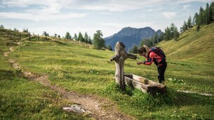 Frau erfrischt sich bei einem Holzbrunnentrog | © SalzburgerLand Tourismus/Michael Grössinger
