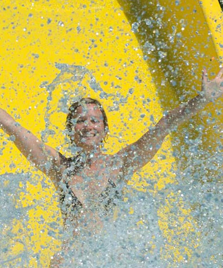 Frau auf Wasserrutsche reist Arme in die Höhe und überall spritzt Wasser | © Tourismusverband Bergheim/Bryan Reinhart