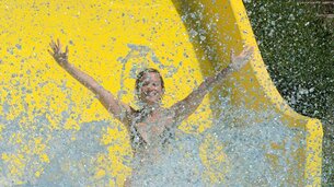 Frau auf Wasserrutsche reist Arme in die Höhe und überall spritzt Wasser | © Tourismusverband Bergheim/Bryan Reinhart